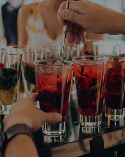 People preparing red cocktails with berries in tall glasses.